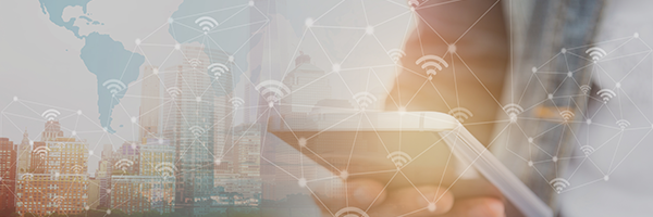 Closeup of a businessman holding a tablet with a city skyline behind him and a map of the world superimposed on top.